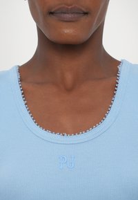 Svijetloplava rebrasta majica bez rukava s dragocjenim okovratnikom i suptilnom "PJ" vezom u odgovarajućoj boji.