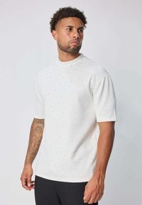 Chemise blanche à manches courtes avec un col rond, ornée de petits points multicolores, texture lisse et coupe décontractée.