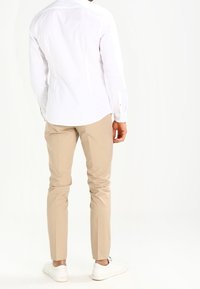 Biała koszula z guzikami, beżowe slim-fit spodnie i białe sneakersy; gładki materiał, dopasowany krój, czyste linie, w minimalistycznym stylu.