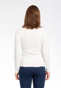 Maglietta bianca a maniche lunghe realizzata in tessuto morbido, abbinata a jeans in denim blu con tasche posteriori e una silhouette aderente.