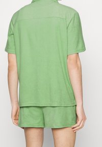 Conjunto de toalla verde que incluye una camiseta polo de manga corta y pantalones cortos a juego, con una textura suave y un corte holgado.