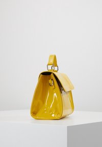 Borsa gialla con una forma strutturata, finitura lucida in vernice, dettagli testurizzati e una maniglia superiore. Presenta una chiusura con pattina magnetica.