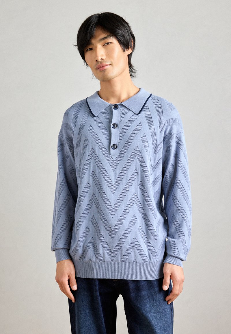 Pull en tricot bleu clair avec un motif en chevrons, doté d'un col, de trois boutons et de poignets et d'un ourlet côtelés.