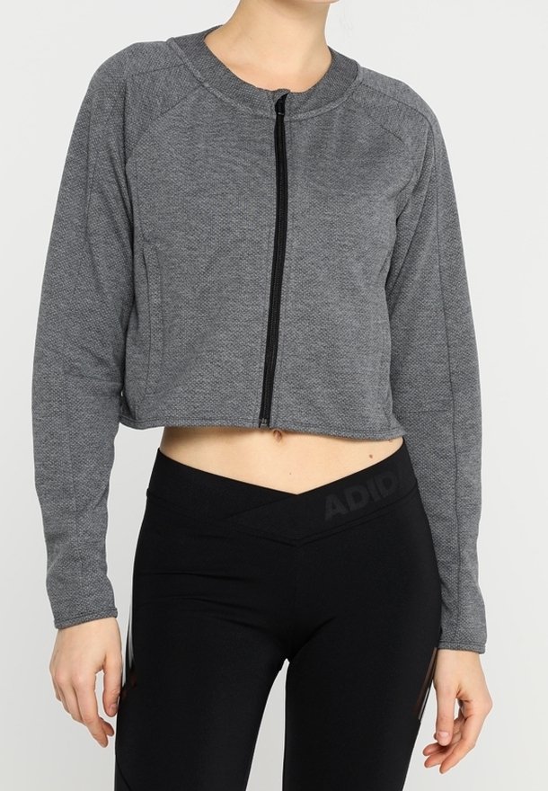 Grå korta zip-up-jacka med en texturerad stoff, med raglanärmar och en svart dragkedja. Tillsammans med svarta leggings med logotyp.