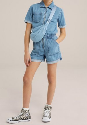 Ensemble en denim bleu clair comprenant une salopette à manches courtes, fermeture éclair sur le devant et ceinture élastique ; associé à des baskets montantes à imprimé léopard.