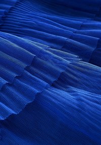 Tissu en maille bleue avec une texture plissée, présentant un design en couches et un motif de tissage fin et ouvert. La couleur est vive et homogène.