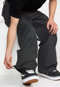 Szare, luźne spodnie z teksturowanej tkaniny, z regulowanym sznurkiem przy mankietach, w zestawie z czarnymi trampkami.