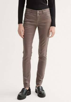 Braune, enganliegende Hose mit glatter Textur, ausgestattet mit einer Doppelknopf-Verschluss und schrägen Fronttaschen. Getragen mit klobigen schwarzen Loafers.