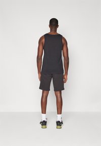 Svart tank topp og shorts, laget av et mykt stoff. Har en uformell passform og minimalistisk design, sammen med svarte treningssko.