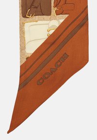 Bufanda de seda con un cálido color naranja, adornada con ilustraciones detalladas de bolsos y accesorios, y un logotipo "COACH" en un tono más oscuro.