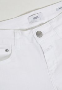 Bílé denimové džíny s uzavíráním na knoflík, poutky na opasek a předními kapsami. Materiál má hladkou texturu a jemné švy.