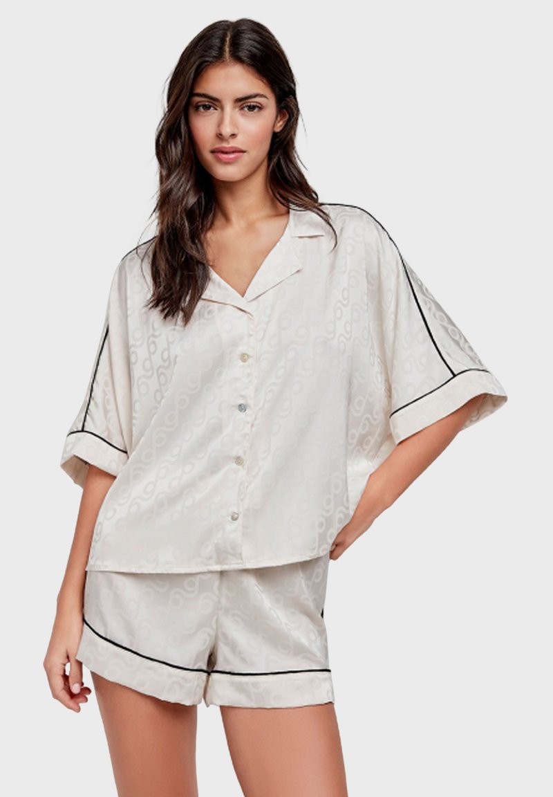 Ensemble de pyjama en satin crème avec un motif subtil, comprenant un haut à boutons à manches courtes et un short à cordon avec des finitions noires.