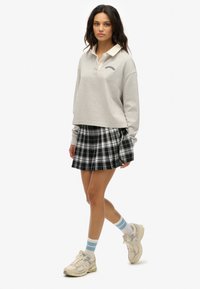 Grijs cropped sweatshirt met een beige kraag, gecombineerd met een zwart-wit geruite plooienrok. Grijs en beige sneakers met blauw gestreepte sokken.