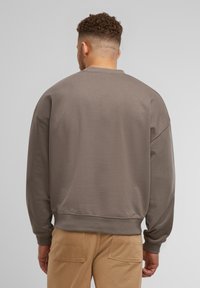 Szary sweatshirt z okrągłym dekoltem, opadającymi ramionami i ściągaczami. Wykonany z gładkiej tkaniny, minimalistyczny design, bez widocznych logo.