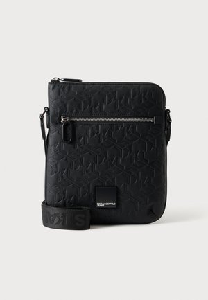 Sac bandoulière en cuir noir embossé avec poche zippée à l'avant, bandoulière réglable, et petite plaque logo en bas au centre.
