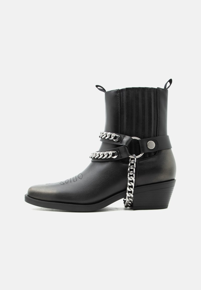 Μαύρο δερμάτινο μποτάκι μέχρι τον αστράγαλο με τακούνι σε στρώσεις, διακοσμητικές αλυσίδες από ασήμι, λουριά, θηλιές έλξης και ραφές διακόσμησης στη μύτη και τον κορμό.