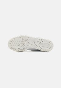 Suela de zapatilla atlética blanca con goma texturizada para agarre, que presenta surcos y un detalle de logo circular, diseñada para estabilidad y tracción.