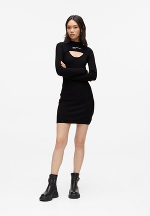Black knit dress with long sleeves, a cut-out neckline, and a fitted shape. Paired with black leather ankle boots featuring hardware accents.
