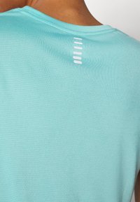 Lichtblauw sportshirt met een ronde hals, gemaakt van een gestructureerde stof, met een rij kleine witte accenten aan de achterkant.