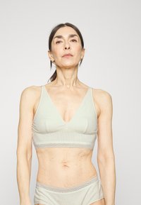Bralette verde-claro com nervuras e design em V. Apresenta rendas na banda e uma textura suave para conforto.
