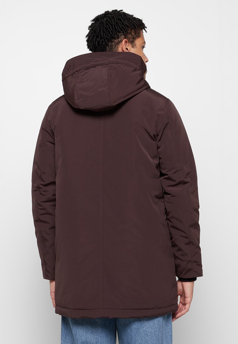 Donkerbruine gewatteerde jas met capuchon, voorzien van een gladde textuur, lange mouwen en een rechte snit. Minimale zichtbare details.