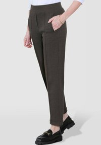 Bruine herringbone broek met een hoge taille, zijzakken en een taps toelopend ontwerp, gedragen met zwarte loafers met gouden details.