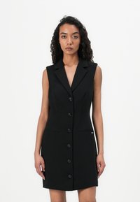 Black sleeveless dress featuring a tailored design, six large buttons, a collar, and two side pockets for a streamlined silhouette.
