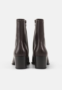 Botas de tobillo de cuero marrón con un acabado liso, que cuentan con un tacón cuadrado, cierre con cremallera lateral y un diseño minimalista.
