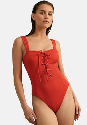 Roter gerippter Badeanzug mit einem quadratischen Ausschnitt, breiten Trägern und einem vorderen Schnürdesign mit Metallösen. Die hoch geschnittenen Beinausschnitte sorgen für eine elegante Passform.