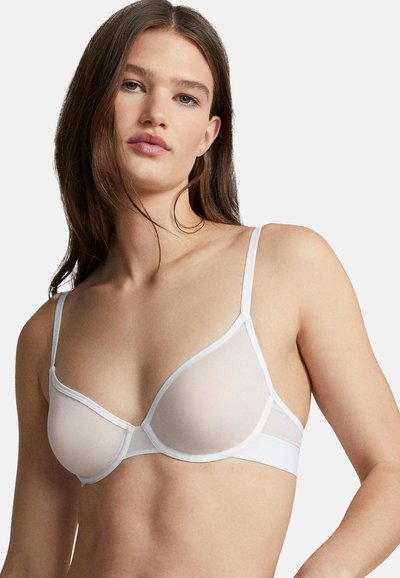 Bílá podprsenka s průsvitnou látkou, všitou kosticí, nastavitelnými ramínky a hladkým pásem. Má minimalistický design bez dalších vzorů.