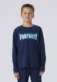 T-shirt à manches longues navy avec le mot "FORTNITE" en lettres bleu glacial évoquant des flammes. Fabriqué en tissu doux et léger, il présente un col rond et une coupe décontractée.