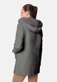 Abrigo de lana gris con capucha de pelo sintético. Presenta una textura suave, un ajuste holgado y un diseño sin costuras. La vista trasera no muestra cierres o adornos visibles.