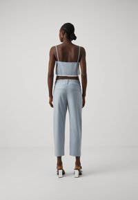 Lyseblå, kort cropped tanktopp med tynne stropper, paret med lyseblå bukser med elastisk midje. Glatt tekstur, minimalistisk design og ingen synlige mønstre.