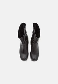 Bottes basses en cuir noir présentant un design élégant, une fermeture éclair, une texture lisse et un bout arrondi. Semelle en caoutchouc plate pour plus de stabilité.