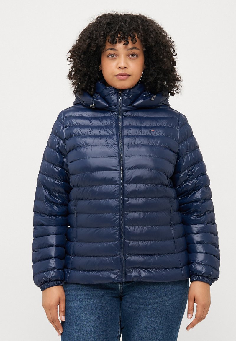 Marineblaue Pufferjacke mit Reißverschluss, Kapuze und elastischen Bündchen. Verfügt über ein gesteppte Design und ein kleines Logo-Akzent auf der Brust.