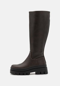Bottes en cuir marron montantes jusqu'au genou avec une semelle noire épaisse et peu de détails de couture. Design épuré avec une texture lisse.