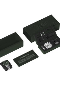 Eine grüne Verpackung zeigt eine Smartwatch mit einem Armband aus Edelstahl, einem schwarzen Display und grünen Akzenten. Enthält zusätzliches Zubehör und eine Karte.