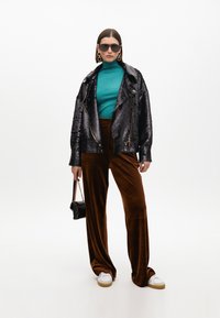 Giacca bomber nera con paillettes, dolcevita turchese, pantaloni a gamba larga in velluto marrone, occhiali da sole oversize e piccola borsa nera. Sneaker bianche.