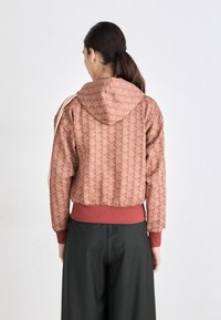 Lett, mønstrete hettejakke i dempede rosatoner med ribbestrikkede mansjetter og kant, med geometrisk design og hette detaljer.