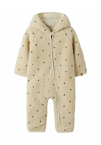Combinaison bébé en polaire de couleur crème avec capuche, fermeture éclair à l'avant et petits motifs en forme de cœur noir disséminés sur le tissu.