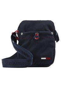 Borsa a tracolla blu navy in tessuto, con un accento rosso, hardware in argento, patch con logo e tracolla regolabile. Design quadrato compatto.