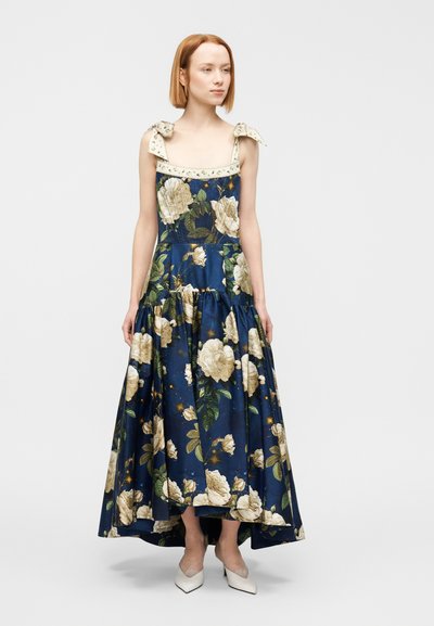 Φλοράλ μαξιφόρεμα σε μπλε ύφασμα με λευκά σχέδια τριαντάφυλλων. Διαθέτει φιόγκους στους ώμους και σχέδιο φούστας με στρώσεις. Φοριέται με λευκά μυτερά παπούτσια.