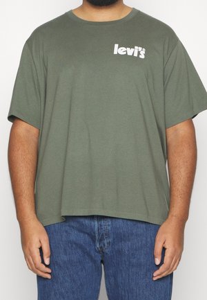 Homme portant un t-shirt Levi's vert olive avec un logo blanc sur la poitrine gauche et un jean bleu, debout devant un fond uni.
