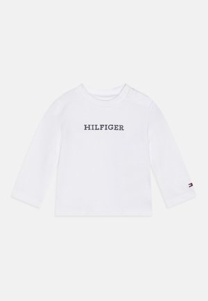 Biała koszulka z długim rękawem dla dziecka z napisem "HILFIGER" na przodzie oraz małą, wyszywaną flagą Tommy Hilfiger na mankiecie lewego rękawa.