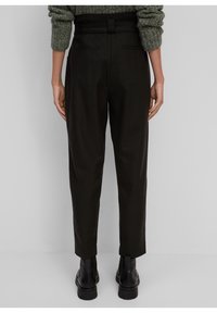 Pantalon noir à coupe ajustée avec une taille haute, dotés de poches latérales et d'une texture lisse, accompagnés de bottines noires à la cheville.