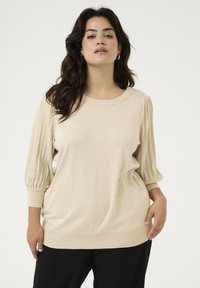 Beige pullover trui met geribde ballonmouwen, een ronde halslijn en een zachte, textuurafwerking. Gedragen met zwarte broek.