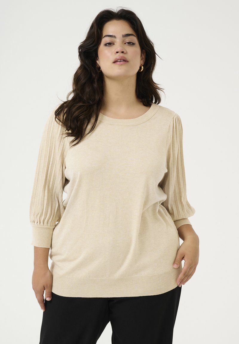 Beige pullover trui met geribde ballonmouwen, een ronde halslijn en een zachte, textuurafwerking. Gedragen met zwarte broek.