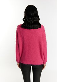 Maglione rosa e peloso con dettagli di perle sulle spalle, vestibilità ampia e polsini a coste, abbinato a pantaloni neri attillati.
