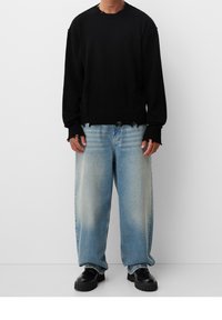 Schwarzer Pullover mit geripptem Halsausschnitt und Bündchen, kombiniert mit hellblauen, zerrissenen weit geschnittenen Jeans und schwarzen Plateauschuhen.