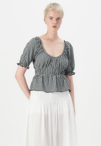 Bluză peplum cu carouri în alb și negru, cu mâneci scurte tip puff, talie elastică și margine volan, asortată cu o fustă plisată albă.